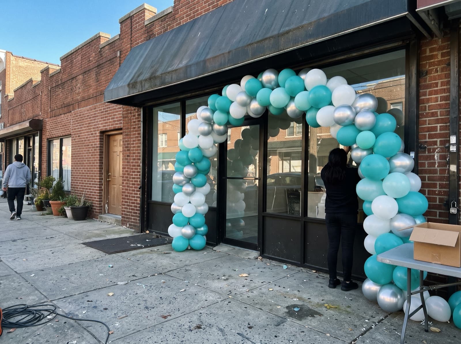 Large balloon arch in teal, white and silver over a shop entrance