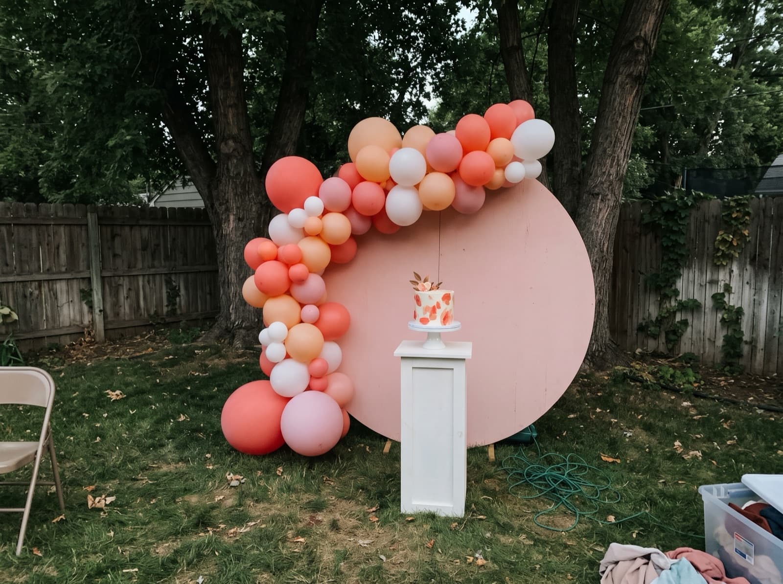 Round blush backdrop with a coral and white balloon garland on a lawn