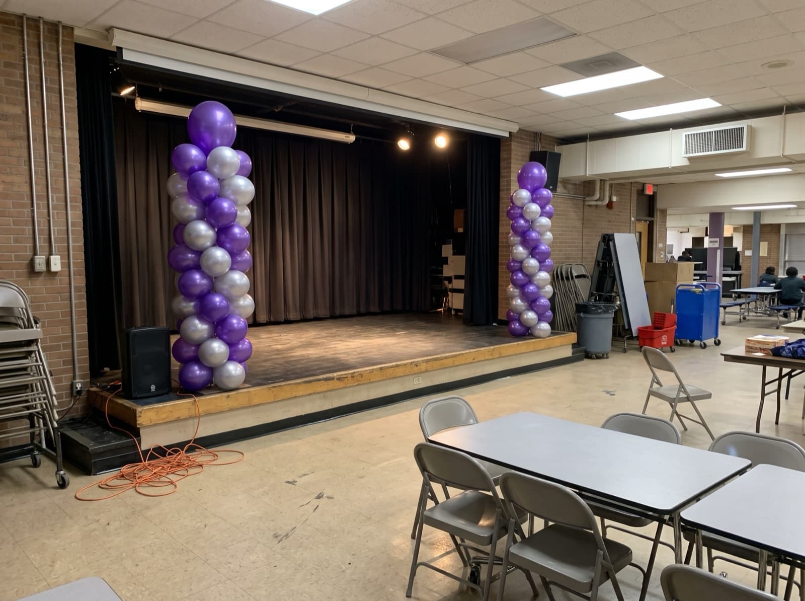 Tall purple and silver balloon columns on each side of a stage