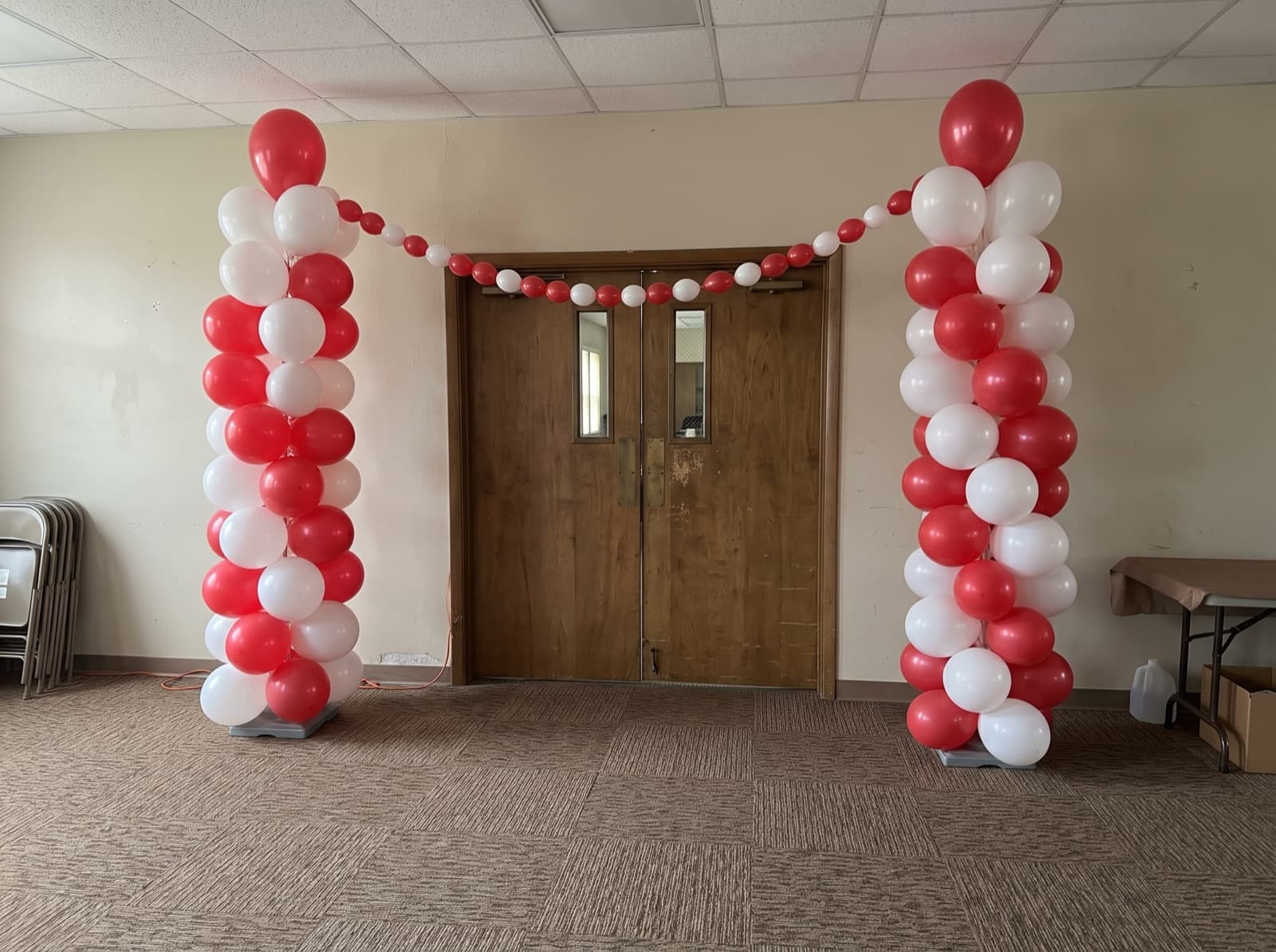 Red and white balloon columns linked by a garland at a church hall entrance