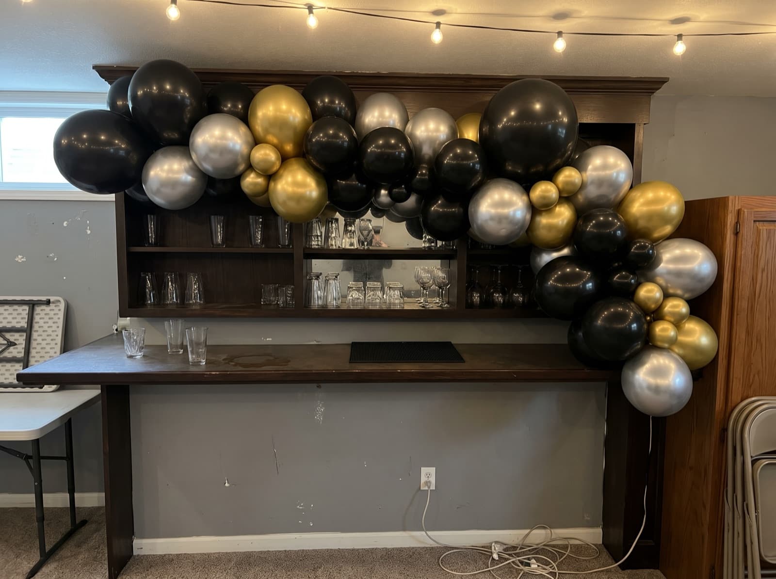 Chrome gold, silver and black balloon garland over a basement bar