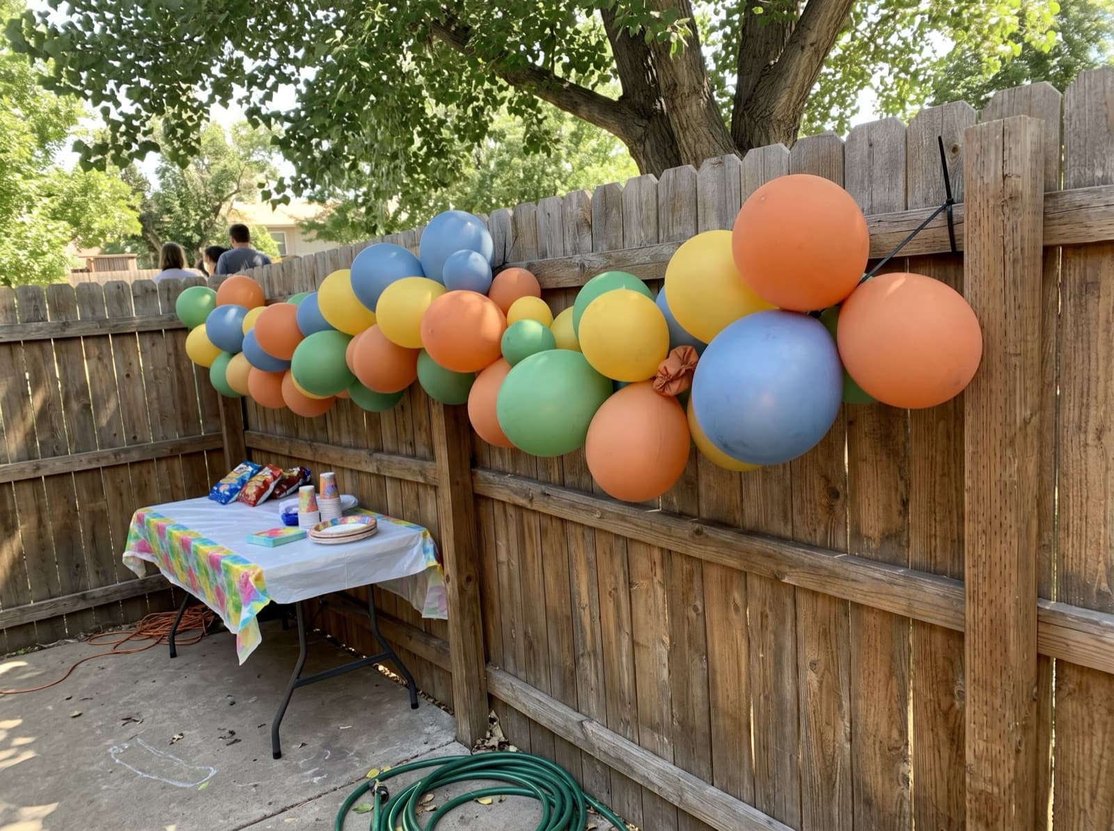 Bright balloon garland on a backyard fence above a kids' party table