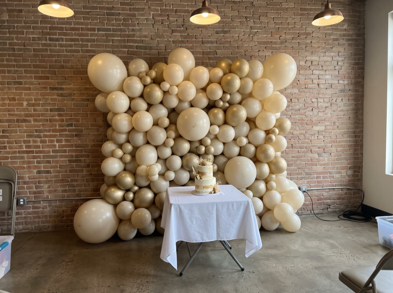 Organic balloon wall in ivory, champagne and gold behind a cake table at a Denver event space